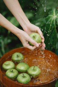 due mani femminili lavano delle mele verdi in un catino d'acqua 